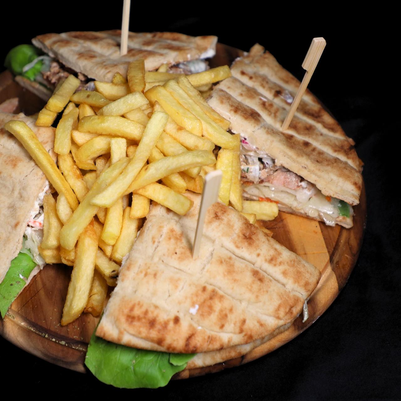 Drei belegte Fladenbrotecken mit Salat und Pommes auf einem Holzteller